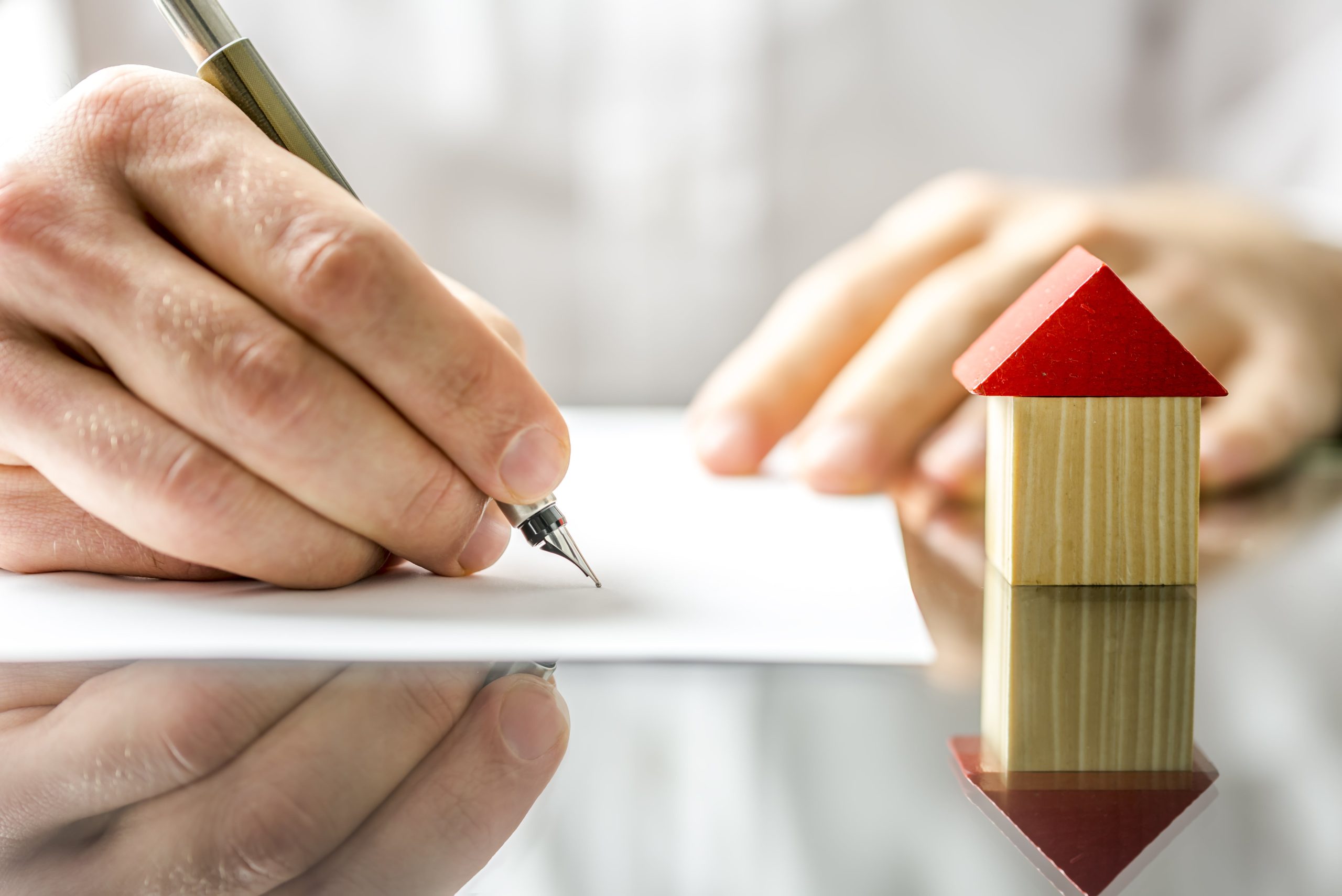 Man signing a document, contract or the deed of sale when buying a new house or selling his existing one with a small wooden model of a house alongside